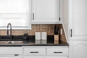 Adorable storage cabinets, well-stocked with kitchen utensils, and a gleaming kitchen sink and countertops, adding charm and functionality to the space.