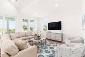 The open living room with a large sectional, flat-screen TV, and balcony access