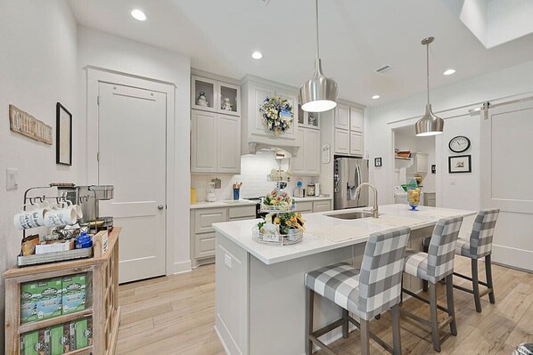A sleek, modern kitchen featuring stainless steel appliances, a cozy coffee station, and a spacious island with stylish counter stools—perfect for cooking or just sipping your morning brew.