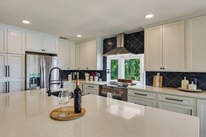 Enjoy cooking in this bright, modern kitchen with high-end finishes and a 6-burner electric stove. The sleek white cabinetry and striking black tile backsplash provide both style and functionality, while the large island with a beautiful countertop makes meal prep a breeze.