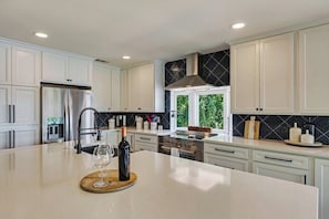 Enjoy cooking in this bright, modern kitchen with high-end finishes and a 6-burner electric stove. The sleek white cabinetry and striking black tile backsplash provide both style and functionality, while the large island with a beautiful countertop makes meal prep a breeze.