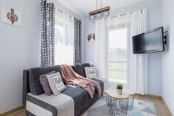 A bright living area with a comfortable sofa, soft throw blanket, and wall-mounted TV, perfect for relaxing in a cozy atmosphere.
