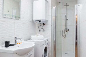 A clean bathroom with a walk-in shower, washing machine, and practical design elements.
