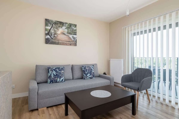 A cozy living room with a modern sofa, armchair, coffee table, and large window allowing plenty of natural light.