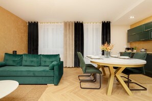A spacious living and dining area featuring a green sofa, a round dining table, and stylish chairs.
