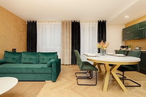 A spacious living and dining area featuring a green sofa, a round dining table, and stylish chairs.