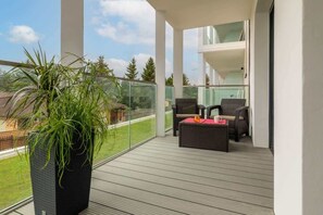 A balcony area with a green plant and comfortable seating, overlooking a peaceful outdoor setting.

