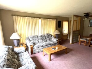 Living room wih couch and loveseat, small dining table, and screened windows.