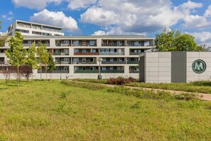 The exterior of a residential complex with modern architecture, surrounded by green grass and trees, creating a peaceful and inviting environment.

