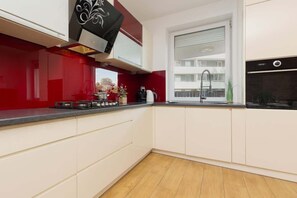 A sleek kitchen with white cabinets, a bold red backsplash, and modern appliances, offering a stylish and vibrant design.

