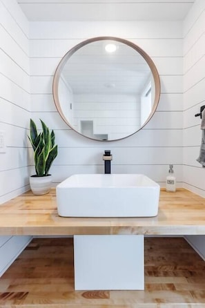 The bathroom features a spacious shower with hot and cold water, fresh towels, and complimentary shampoo. A mirror providing convenience, while ample storage keeps essentials organized. Everything you need for a comfortable and refreshing stay.