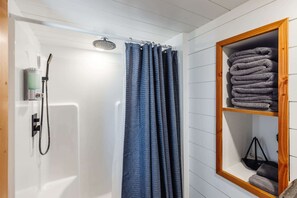 The bathroom features a spacious shower with hot and cold water, fresh towels, and complimentary shampoo. A stylish mirror provides convenience.
