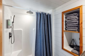The bathroom features a spacious shower with hot and cold water, fresh towels, and complimentary shampoo. A stylish mirror provides convenience.