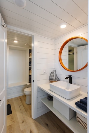 The bathroom features a spacious shower with hot and cold water, fresh towels, and complimentary shampoo. A stylish vanity and mirror provide convenience. Everything you need for a comfortable and refreshing stay!