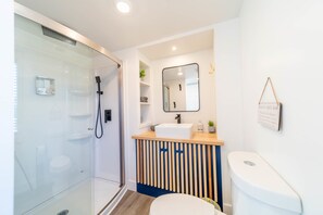 The bathroom features a spacious shower with hot and cold water, fresh towels, and complimentary shampoo. A stylish mirror adds convenience, while ample storage keeps essentials organized. Everything you need for a comfortable, refreshing stay!