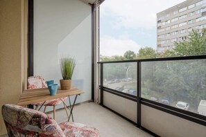 A balcony with a glass railing, a small table, and a plant, offering a relaxing outdoor space with a view.

