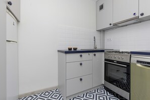 A compact kitchen with white cabinets, black countertops, and patterned floor tiles, blending functionality with modern design.

