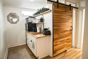 In the small kitchen area, you can find essential appliances such as a coffee maker, microwave, refrigerator, and toaster oven. The space is equipped with necessary dishes and utensils, ensuring functionality despite its compact size.




