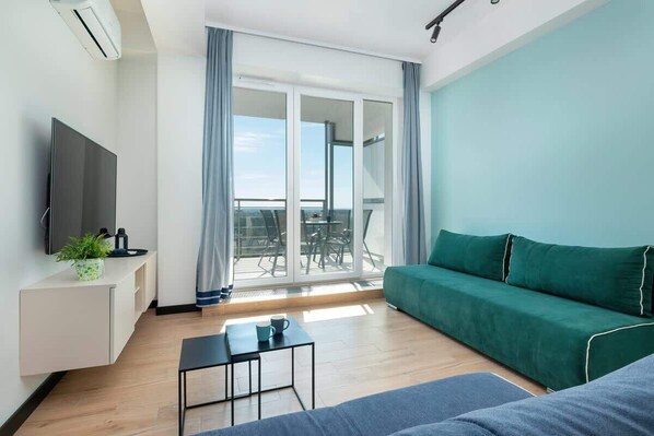 A modern living room with a green sofa, a minimalist coffee table, and large windows offering plenty of natural light.

