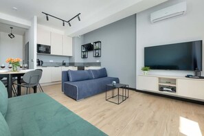 Another angle of the living room featuring the green sofa, a TV, and access to the balcony, creating a bright and airy space.

