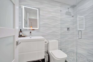 Bathroom has floor to ceiling tile, a standing shower, and an LED vanity mirror for a spa-like experience.