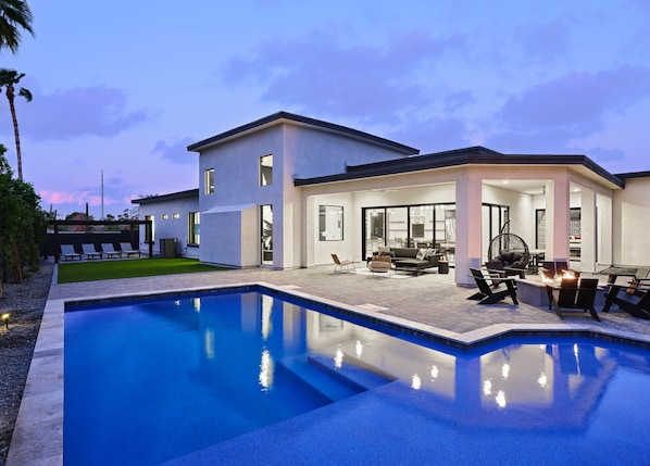 Stunning private yard with sparkling pool, sun loungers, lawn space, covered patio with lounge area, covered outdoor dining area, fire pit, and built-in BBQ grill!