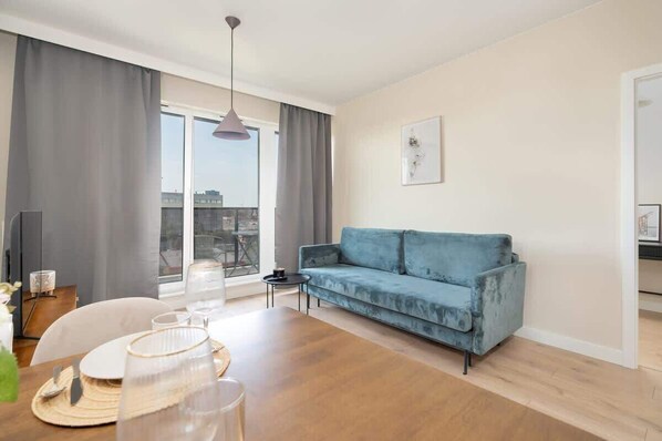 A bright living room with a blue sofa, a small coffee table, and large windows with sheer curtains, creating a modern and inviting space.
