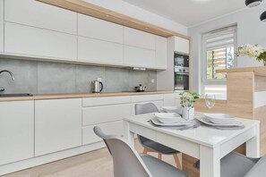 A modern kitchen with white cabinets, wooden accents, and a small dining area, designed for practicality and style.
