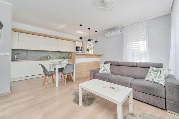 A bright and spacious living and dining area with a gray sofa, a coffee table, and a dining table, complemented by natural light.
