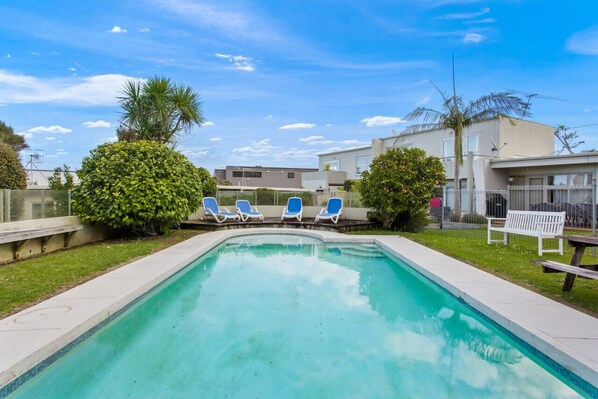 The apartment complex features an expansive on-site pool, deck chair recliners, and a picnic table.