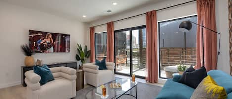 Bright open living space featuring SMART flat-screen TV, designer furnishings, and patio entrance with pool view.