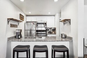 Kitchen bar: three bar stools, bridges the living room and kitchen, granite countertops, stainless-steel appliances, wide range of cookware