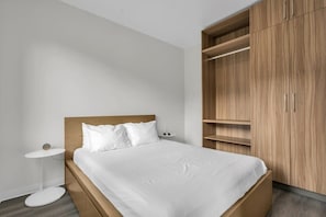 The private bedroom boasts a queen-size bed with two nightstands on either side, a tall closet and shelving space for storage, and a mounted flat-screen TV.
