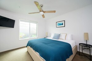 The master bedroom features a flat-screen TV, a ceiling fan, and a luxurious mattress.