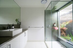 Large bathroom with an immense mirror, sink, additional storage cabinets, a starter kit of toiletries, and luxurious towels.