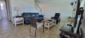 Living room with 65" smart TV, comfortable sofa & recliner, natural light.